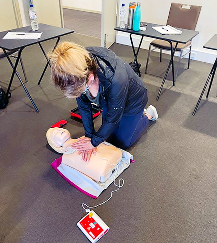 A first aid student crosses one hand over another to perform CPR on a manikin